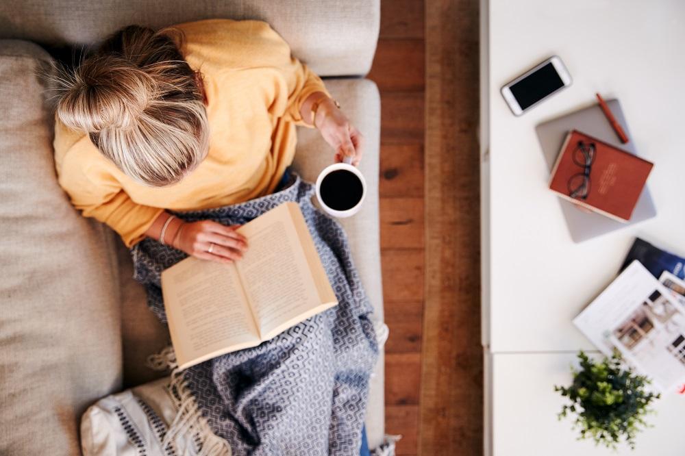 person reclining on a couch while reading and drinking coffee, seen from above