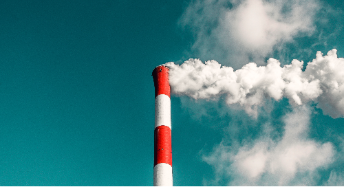 Red and white smokestack billowing smoke against a blue sky.