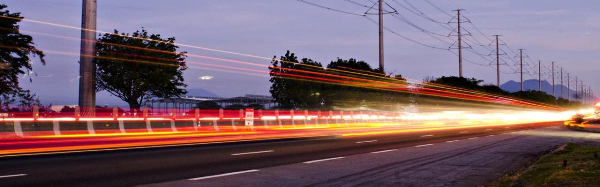 Long exposed lights from a vehicle on a road, power lines along the side of the road.