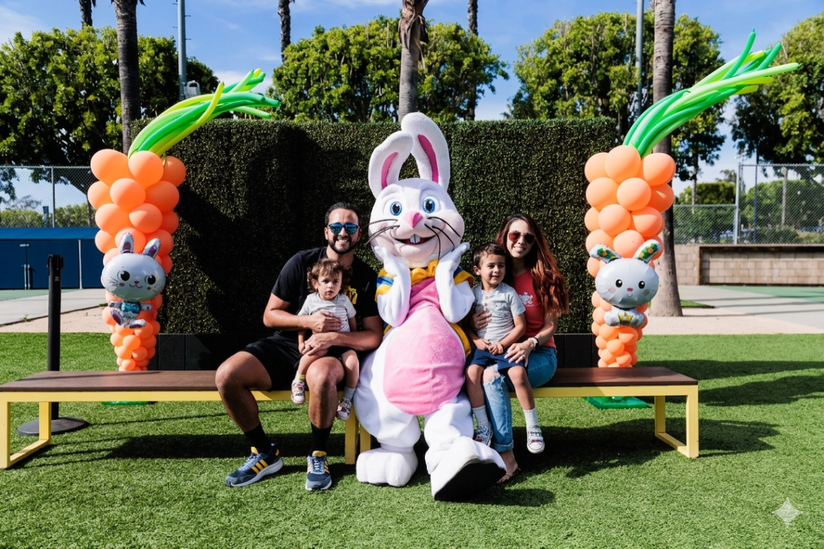 Families sit on a bench posing with a large bunny mascot, surrounded by festive balloon decorations.