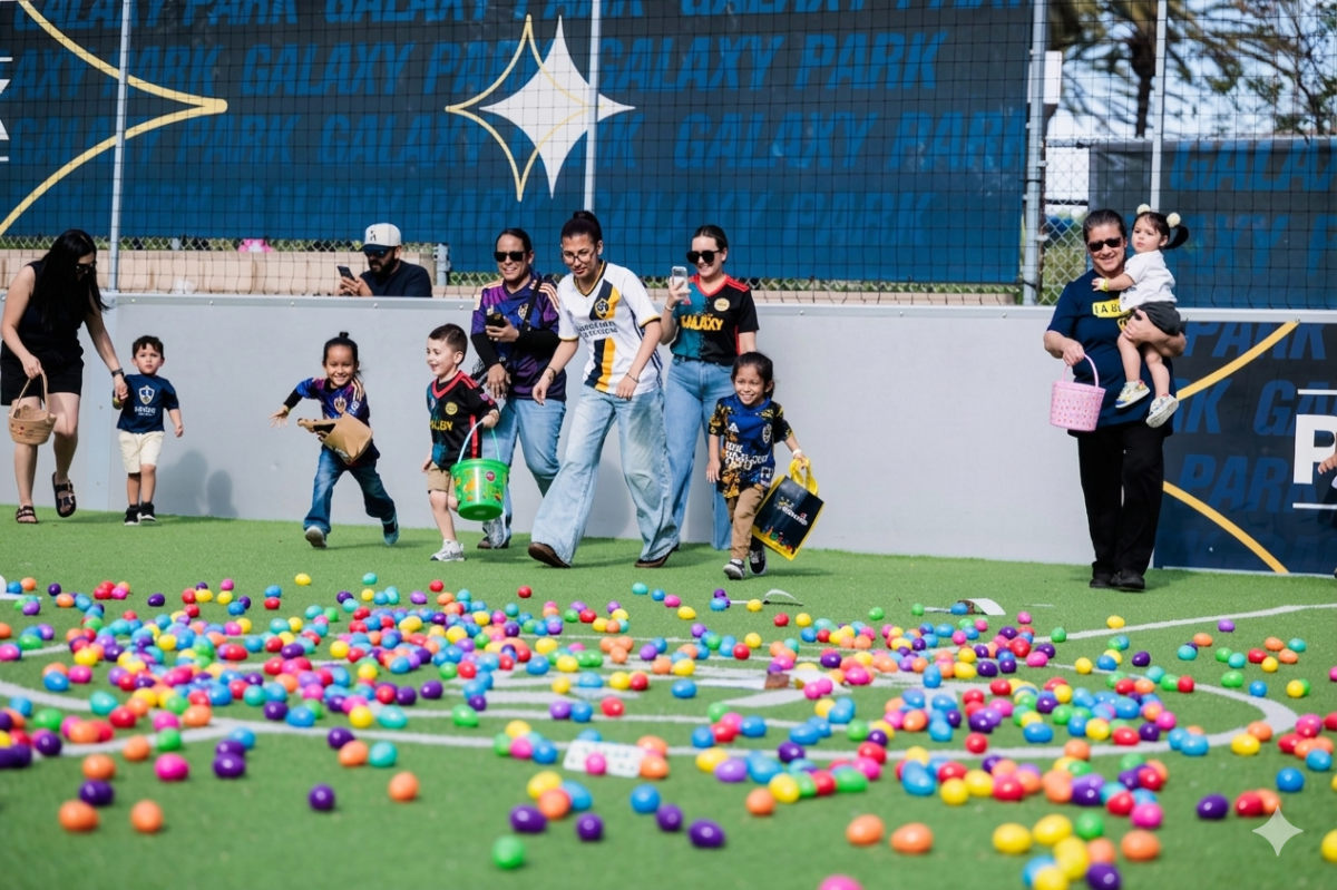 Children run across a turf field toward colorful eggs during a community egg hunt.