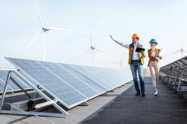 2 workers walk amongst solar panels and wind turbines