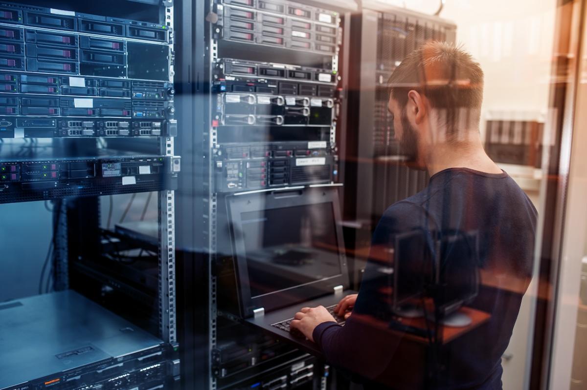 A person with a laptop working in a server room.