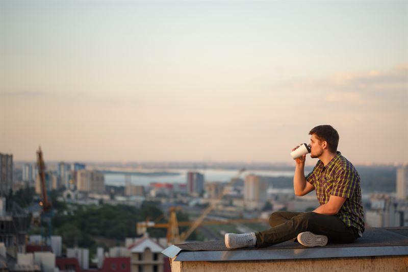 Man sitting on a rooftop drinking from a paper cup.