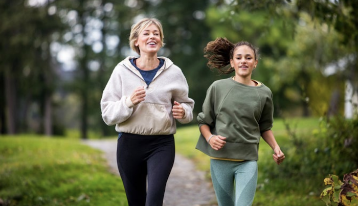 Two women running in a park with trees and grass.