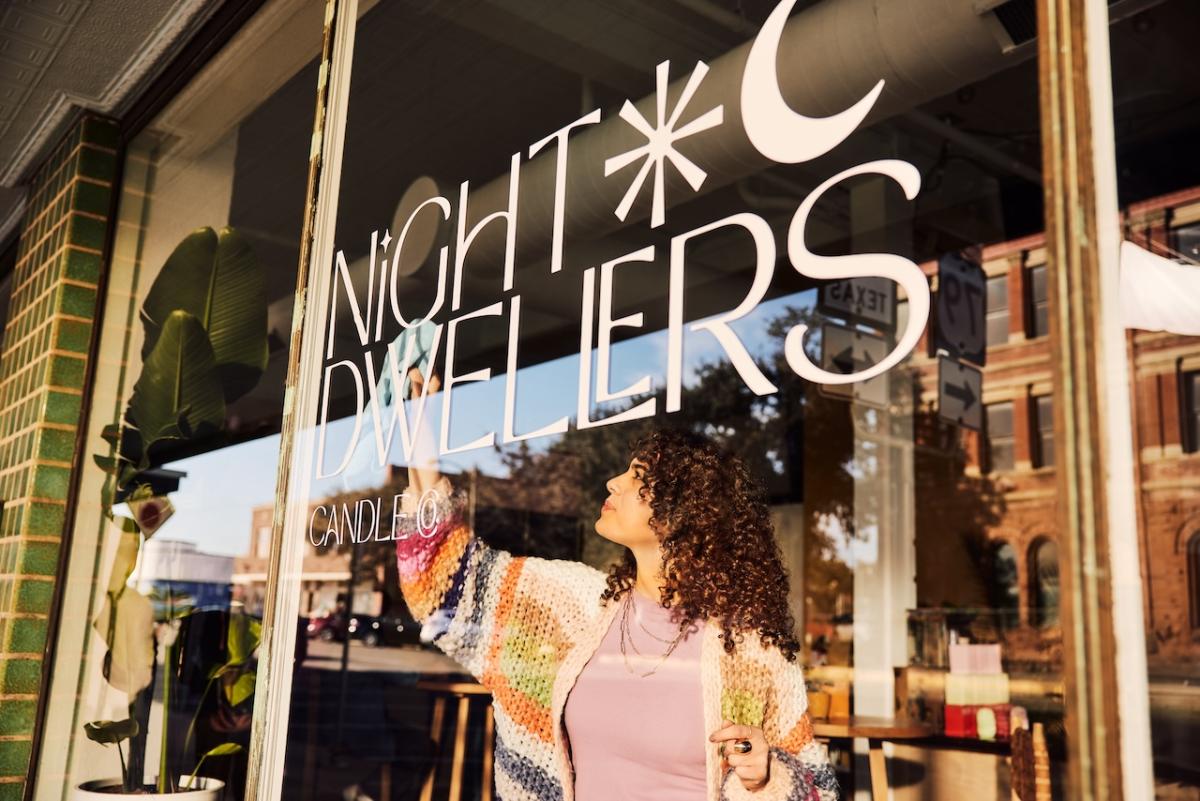 A person cleaning a window of a store called Night Dwellers.
