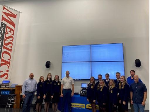 The simulator display will serve as a centerpiece in agricultural education. By integrating the technology into the classrooms, CNH Industrial seeks to cultivate an interactive learning environment for the future farmers of America. Staff an students stood either side of the Precision Agriculture education simulator