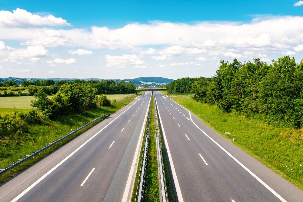 A road stretching off into the distance under a sunny sky with green grass and trees on either side