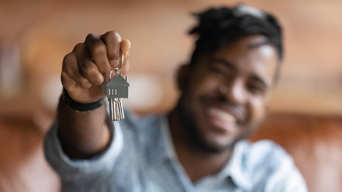 A person of color is holding a key chain with house keys and is smiling.