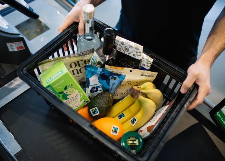 An assortment of Fairtrade certified products in a grocery basket, including bananas, avocado, and tea. 