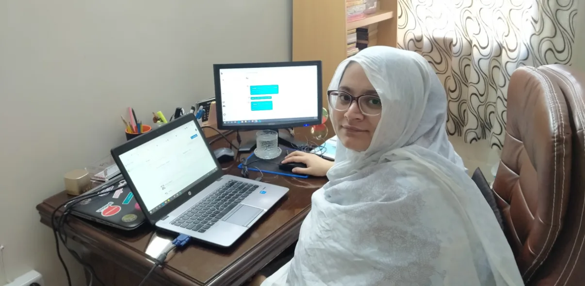 Faiza Yousuf sitting at a home office with a laptop and monitor