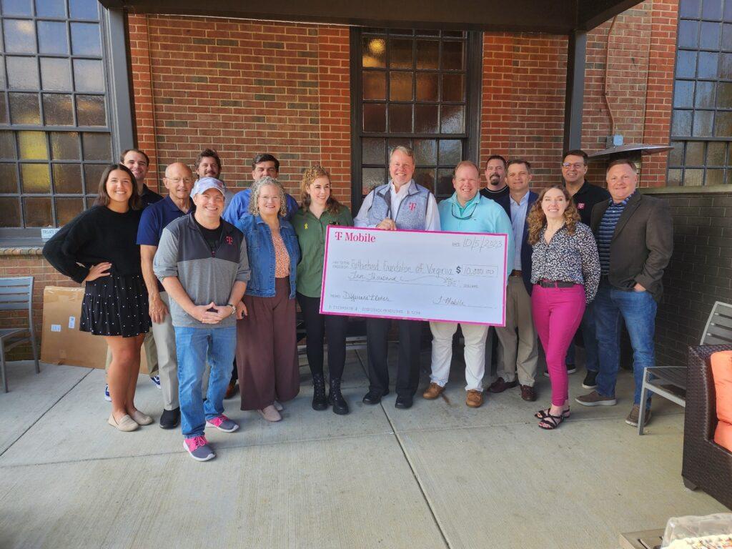 A group of people posed with a large check. A brick building behind them.