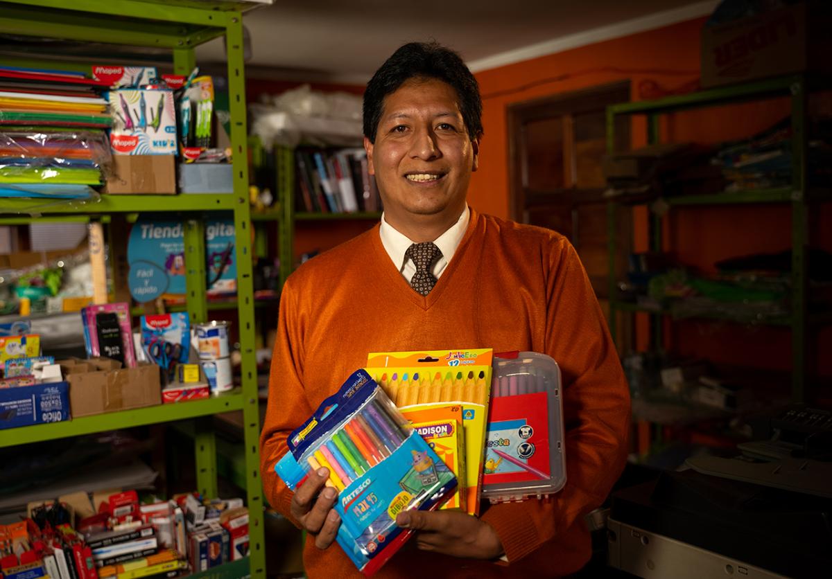 Fernando holding art supplies. Shelves of art and office supplies behind him.