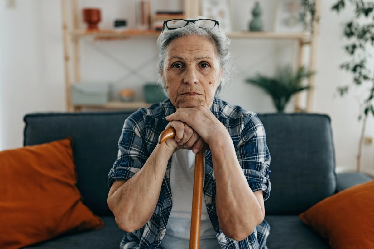 Woman seated on a couch holding her cane.