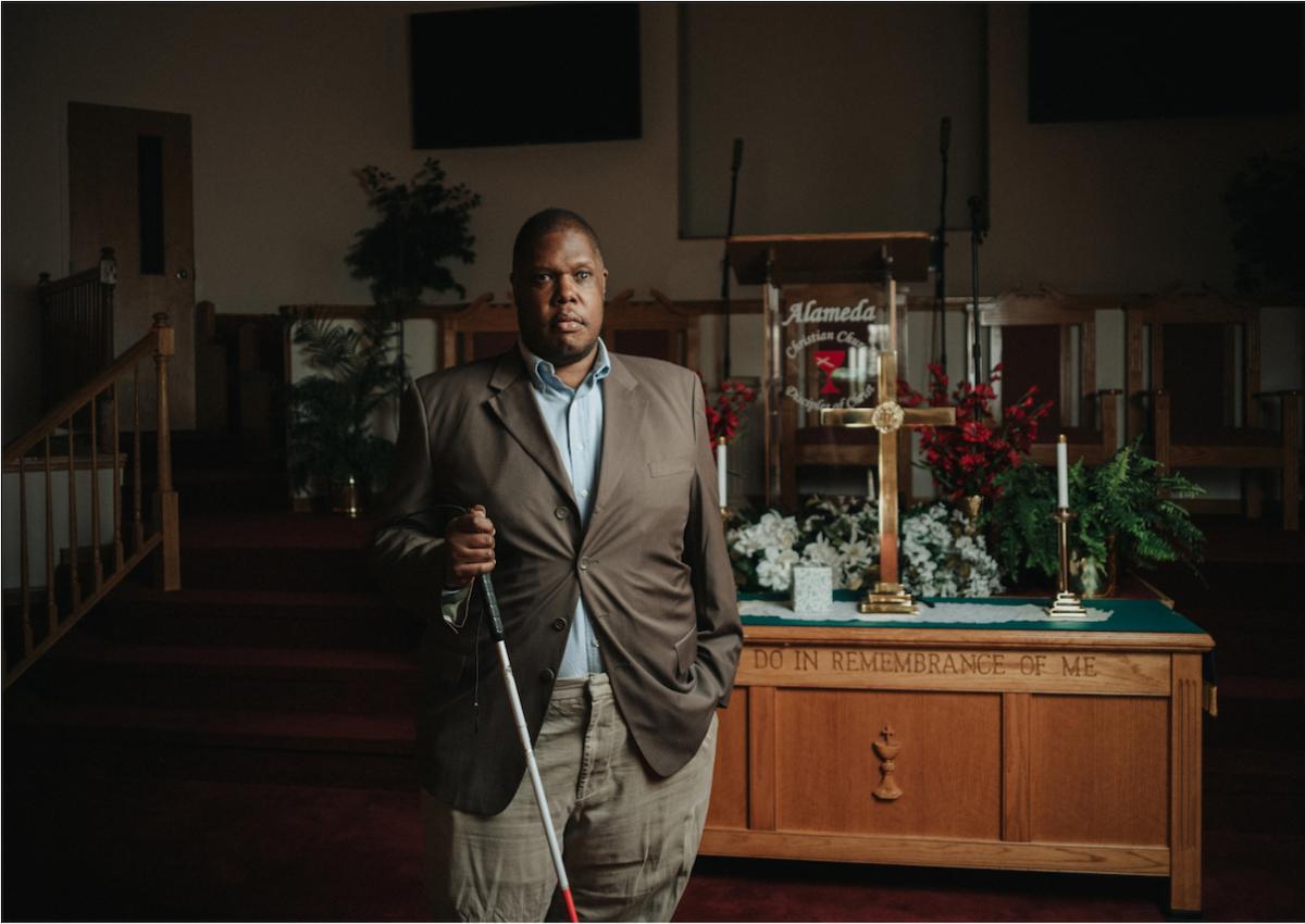 Photo of Jonathan; he is holding a walking stick as an aid to his blindness.