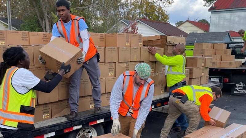 Volunteers wearing safety vests unloading boxes off a trailer.