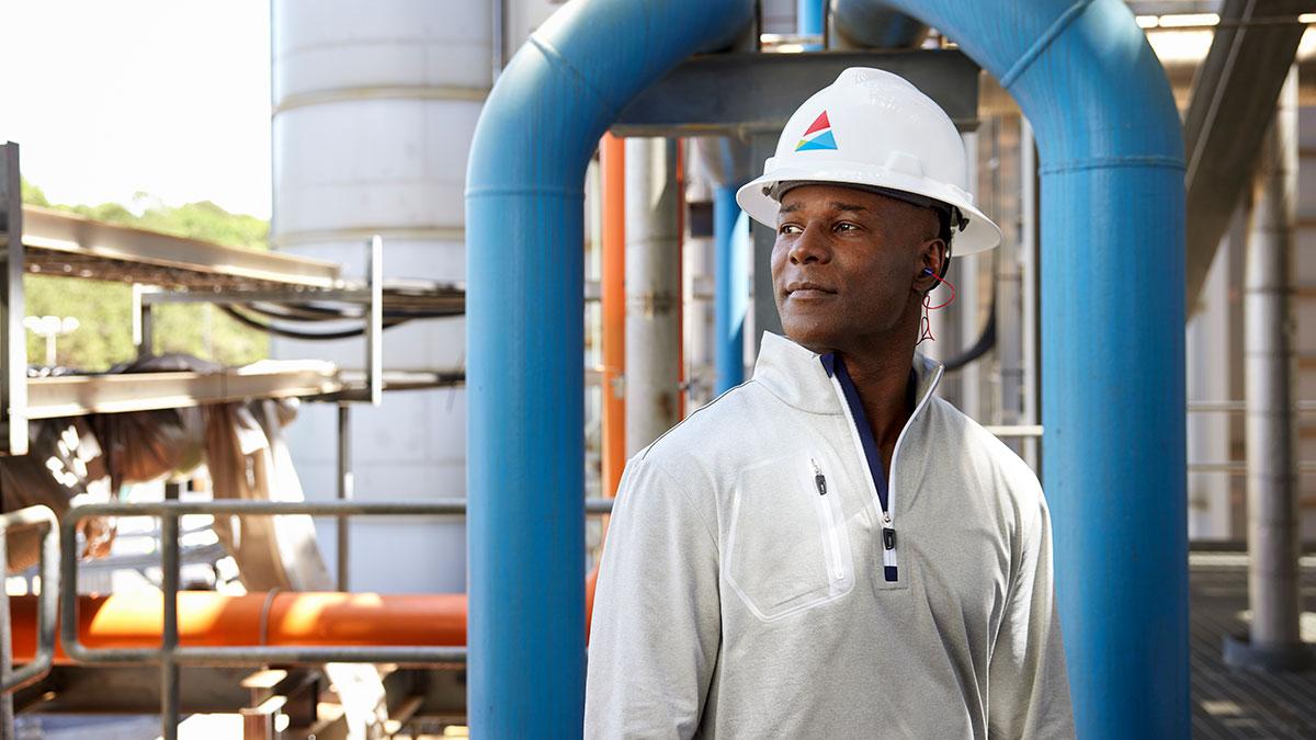 A person in a southern company logo hard hart standing underneath blue industrial piping outside.