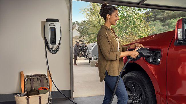 woman in a garage charging a red truck with a wall-mounted cord