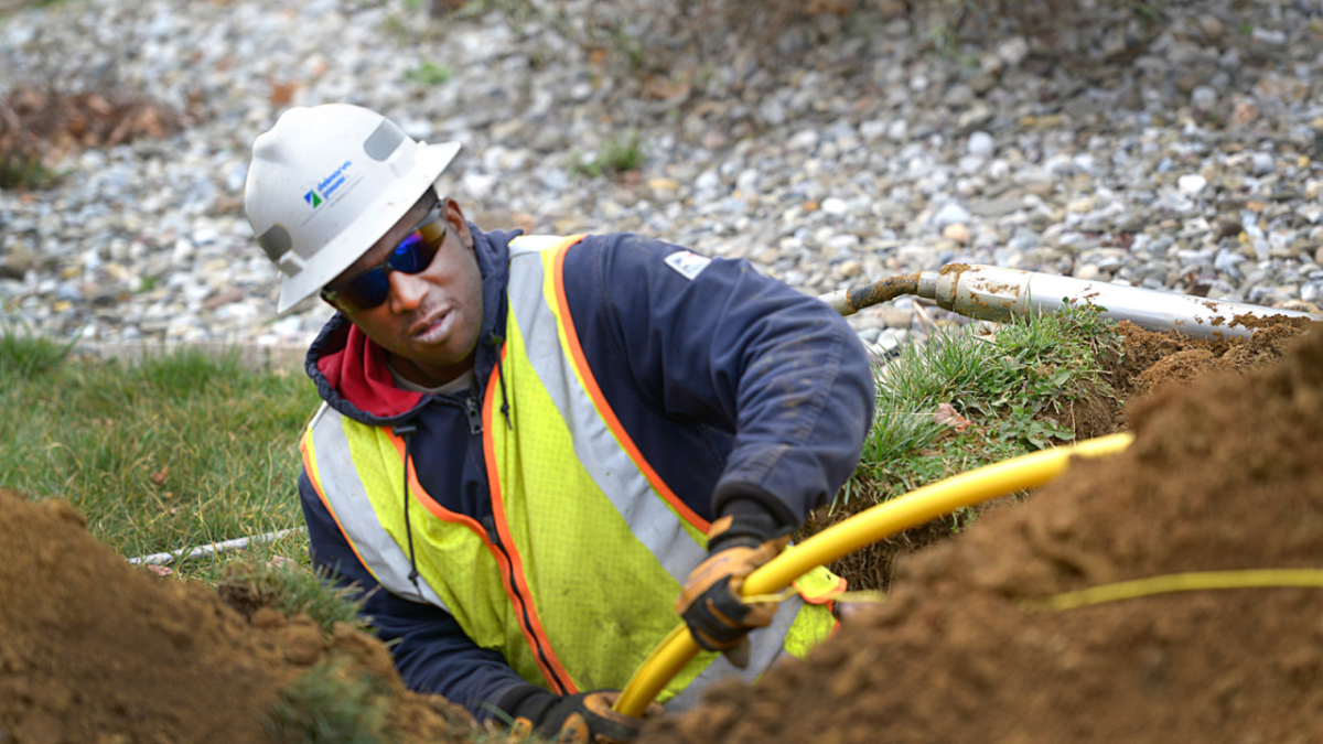 A utility worker pulling a yellow tube through the ground.