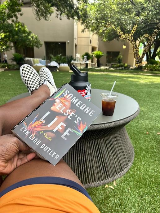 Geoffrey Brown reading a book in his back yard with his feet on a table.