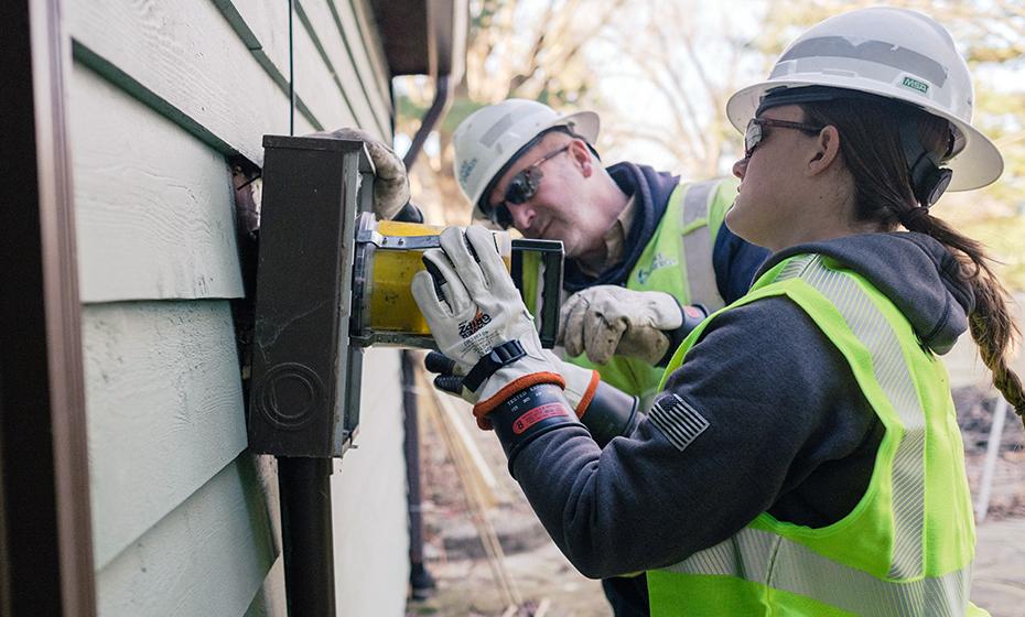 Georgia Hummel working on an electrical box on the outside of a building.