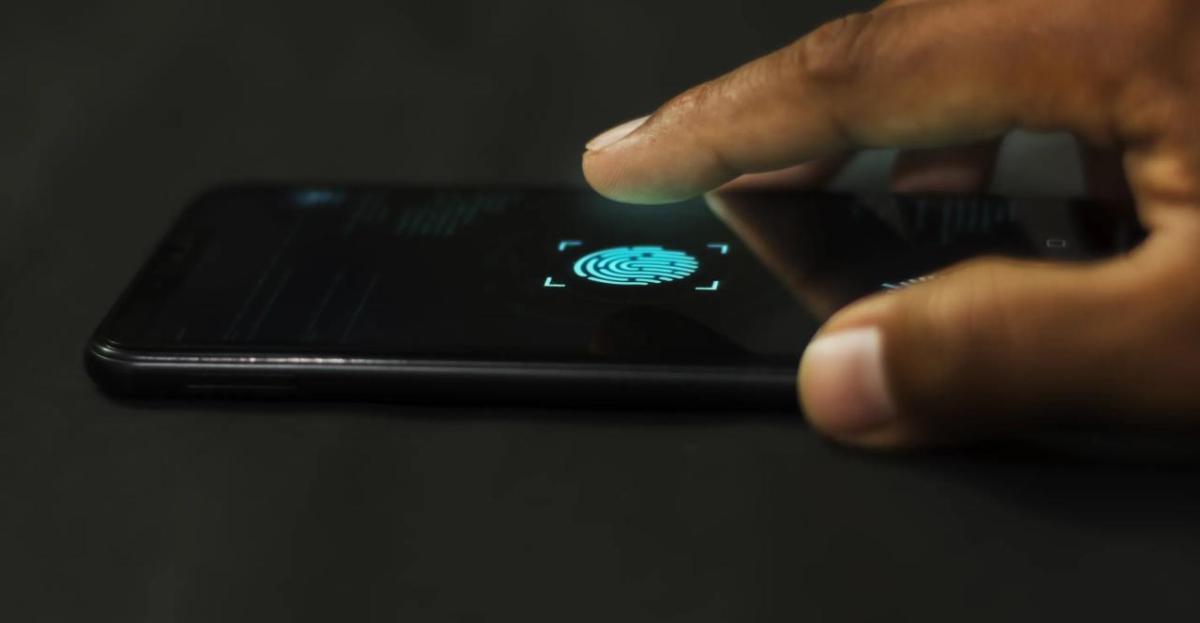 A close-up of a finger poised to tap a fingerprint scanner icon on a smartphone screen, indicating biometric authentication.