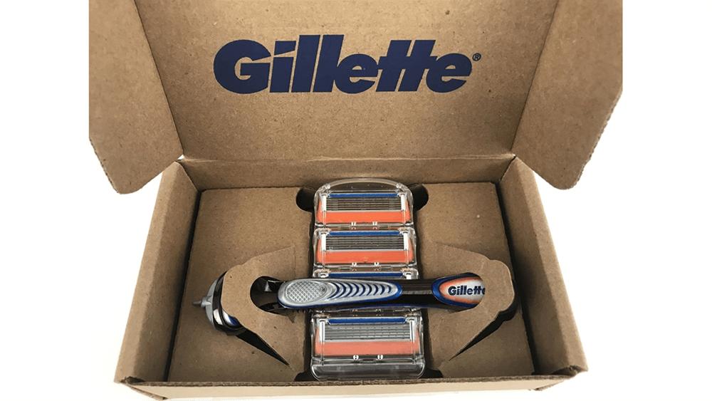 An open cardboard box with Gillette logo on the inside. A razor handle and cartridge refills packaged inside.