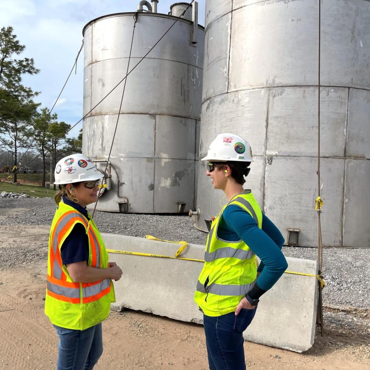 Two women stood talking to each other wearing hi-vis vests and safety hats 