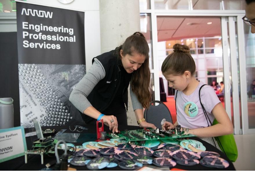 Grace Doepker at an Engineering professional services stand showing a young child some equipment