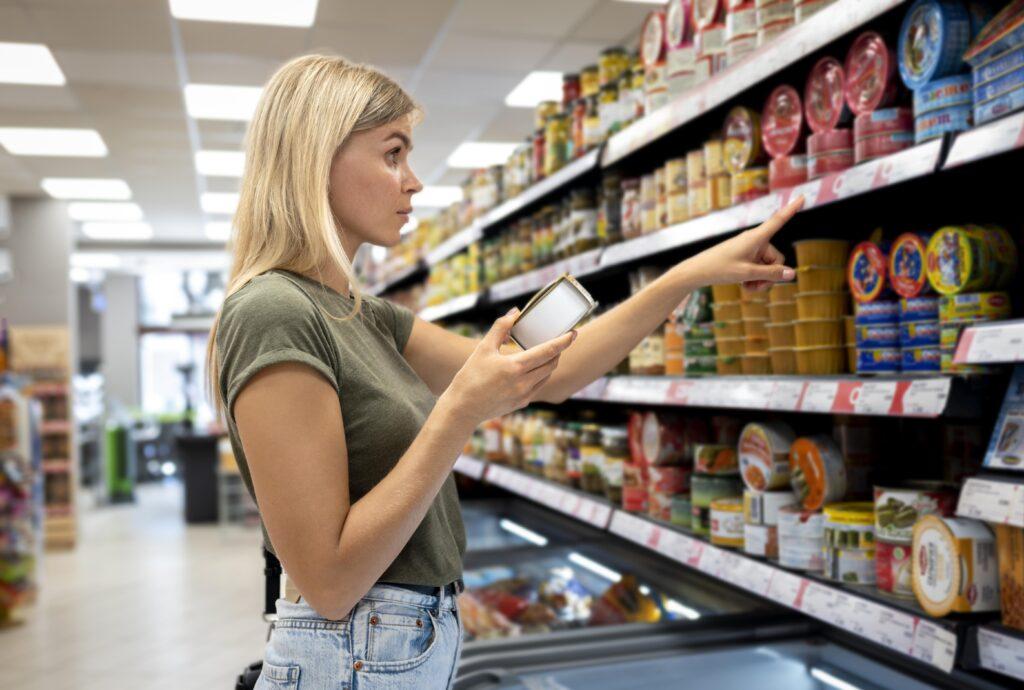 A woman checking prices and information tags on a shelf in a supermarket.