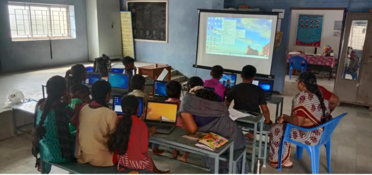 classroom of students sat at tables working on laptops 