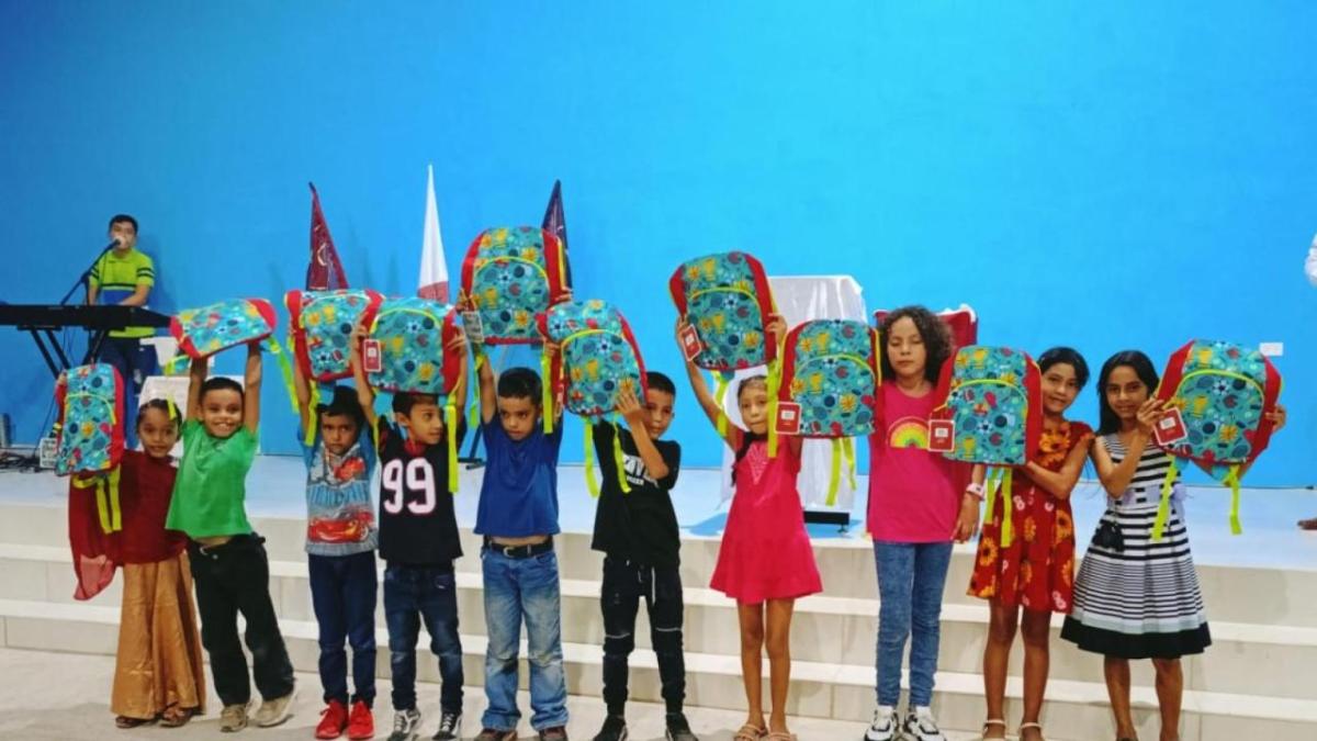 Group of children stood in a line in front of a blue wall holding up matching bags