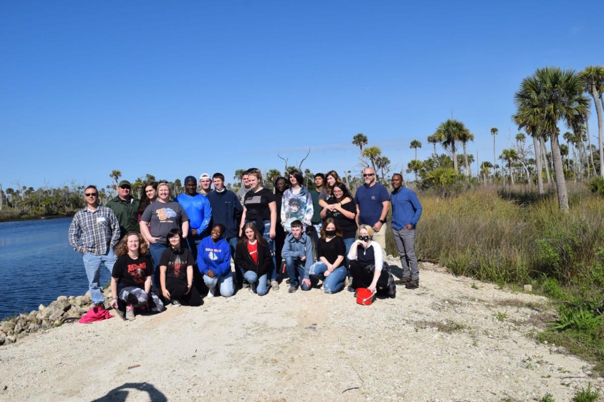 group of students and adults on the bank of a river