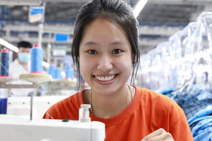 Female worker, smiling, behind a sewing machine.