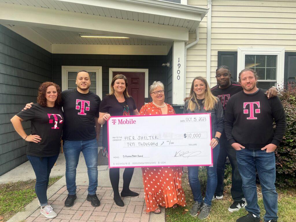 A group of people posed with a large check. A home behind them.