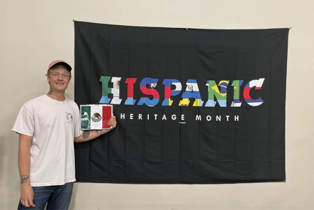 a person standing by a "Hispanic Heritage Month" Flag, holding a smaller Mexican flag.