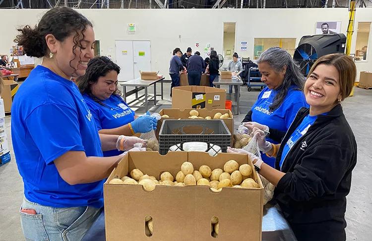 Volunteers in a warehouse packing potatoes from a box.