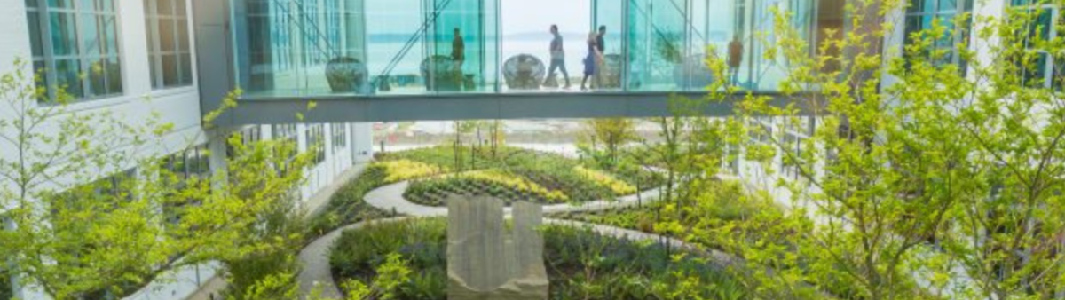 An office building with glass walkway over a lush green courtyard.