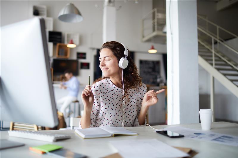 A woman seated at her desk with headphones on.