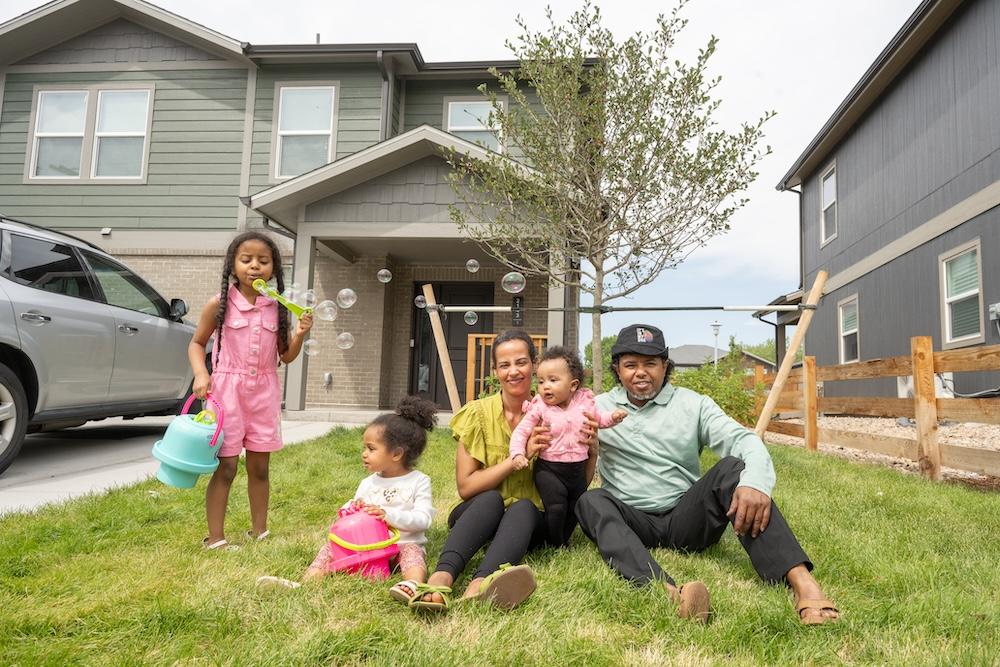 Family of parents and three children sitting in front of house blowing bubbles