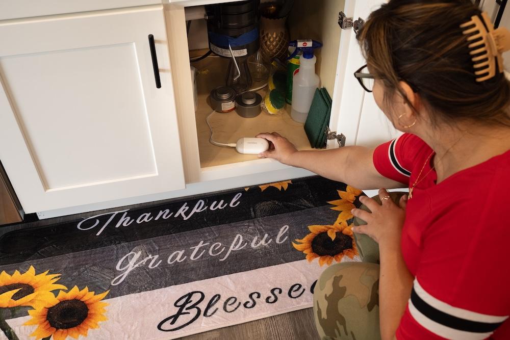 Home owner positioning water leak detector under kitchen sink