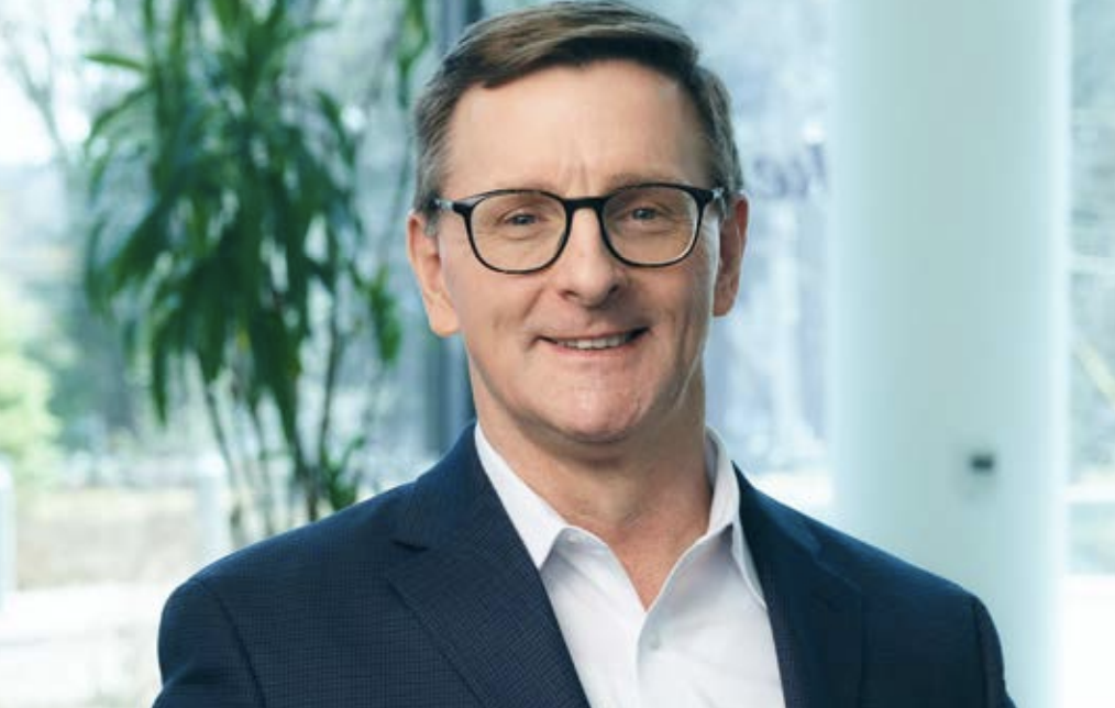 Headshot of a person wearing glasses, stood in front of a plant