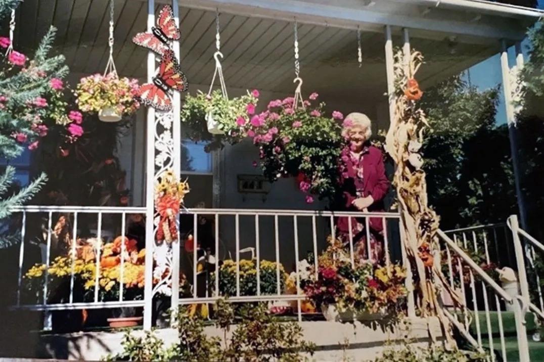 Rodrique's Mom on her front porch surrounded by hanging flower pots and baskets on the floor