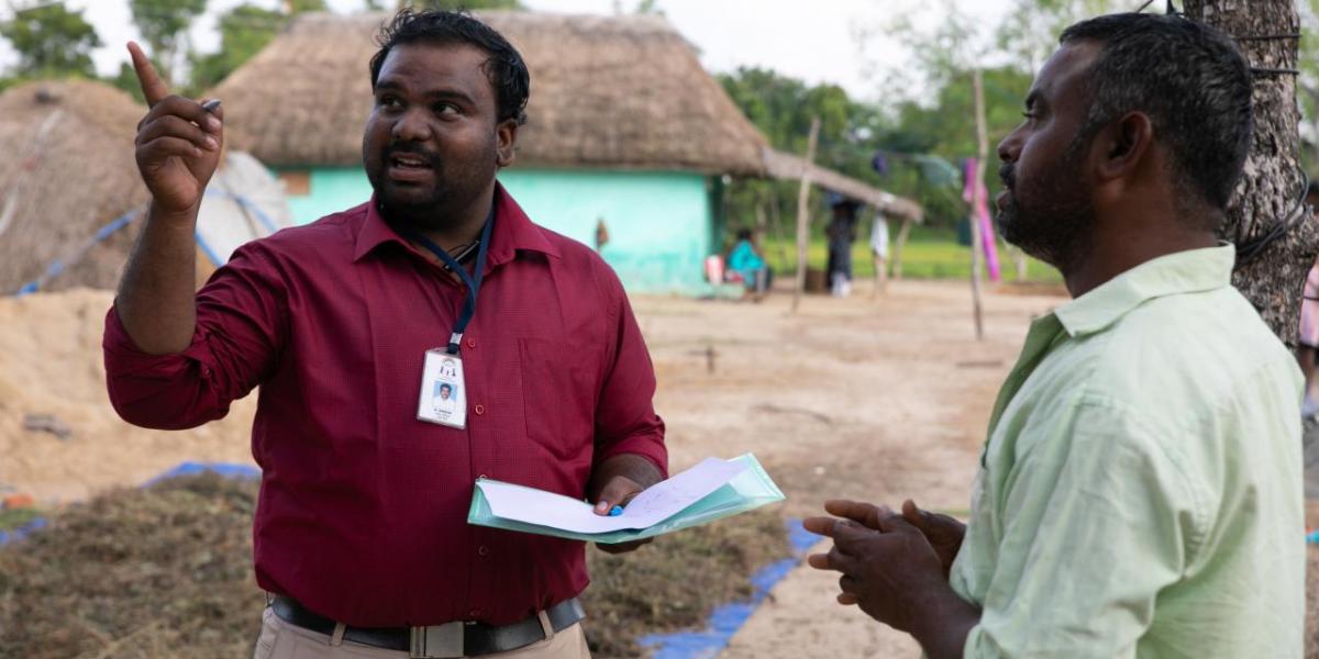 a person wearing a name badge and holding papers points away, another person in front of them