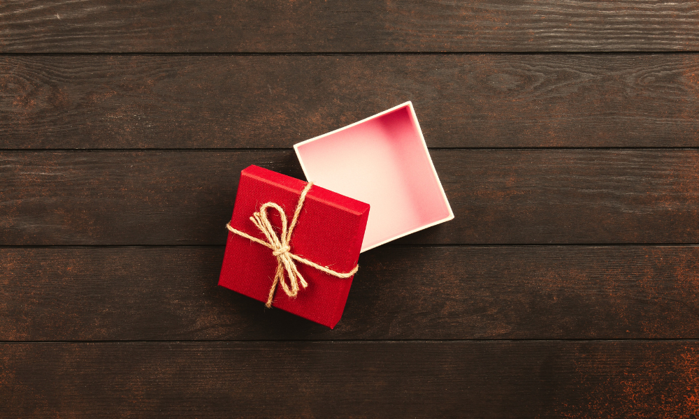 A small, red, square gift box sits opened on a dark wooden table.