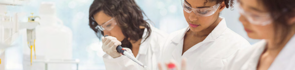 Three people in protective lab gear. One holds a pipette.