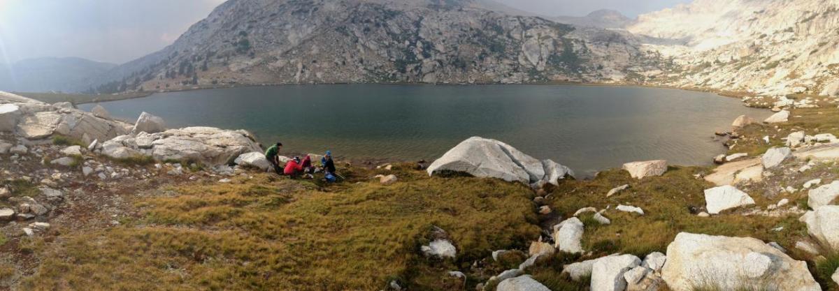 People at the edge of a body of water in mountainous terrain.
