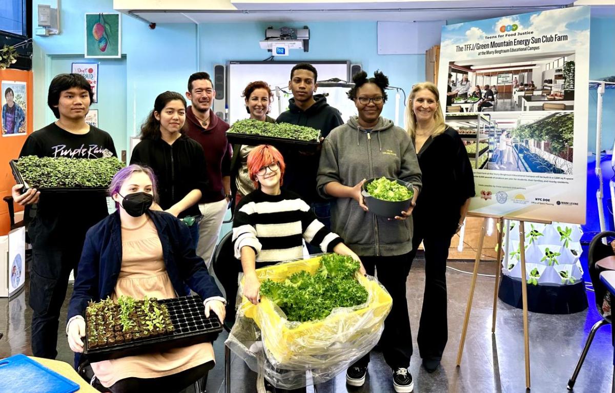 Students and organizational members pose in a high school classroom in front of hydroponic farm setup.