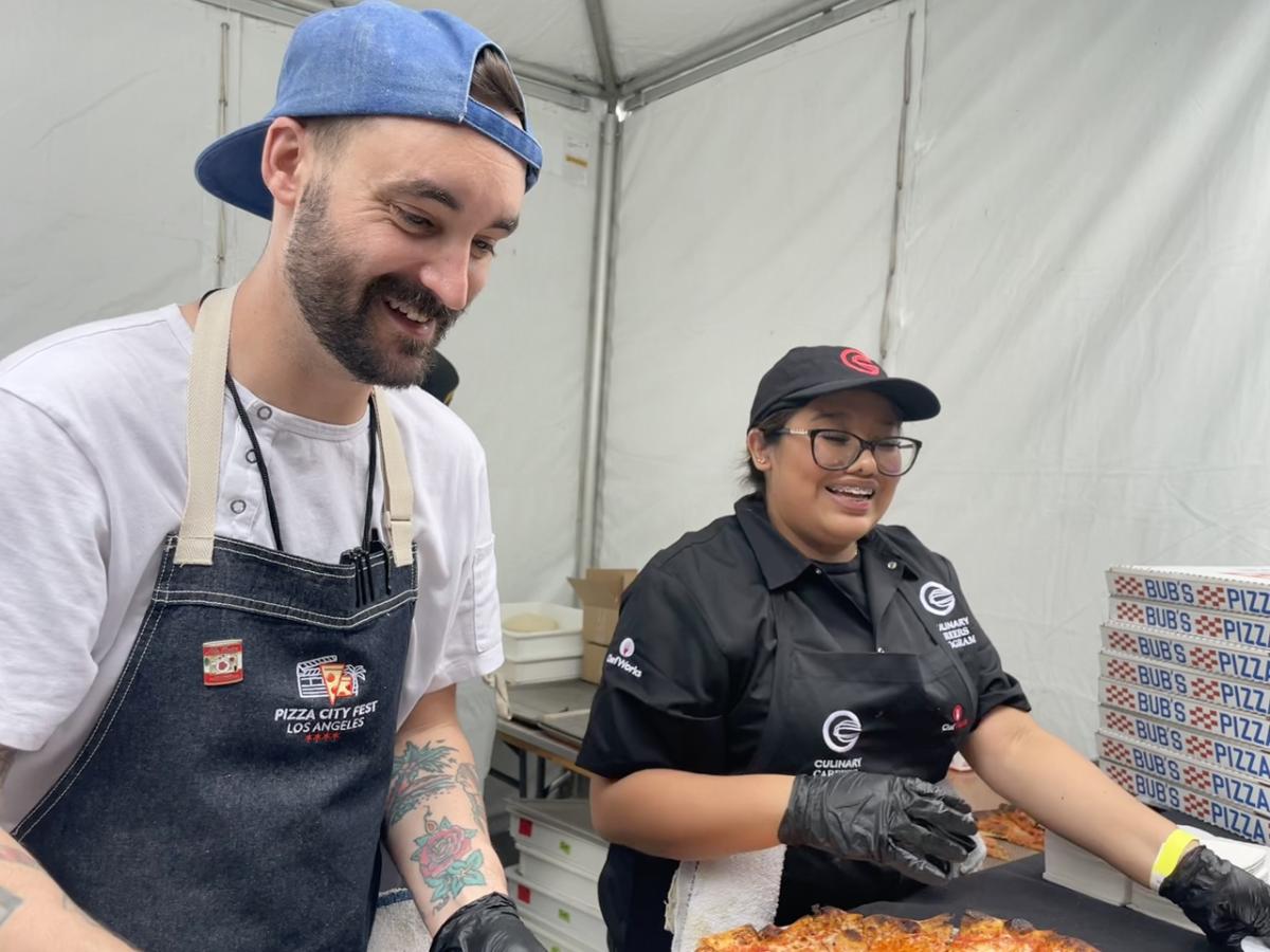Chef and Culinary Careers Program participant slice pizza together at a food festival booth.