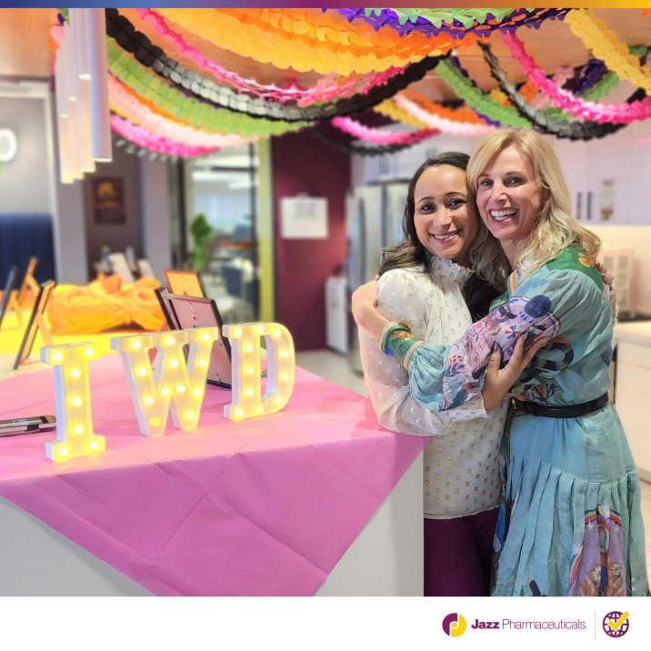 Two people hugging next to a table decorated and IWD letters lit up. Colorful streamers on the ceiling.